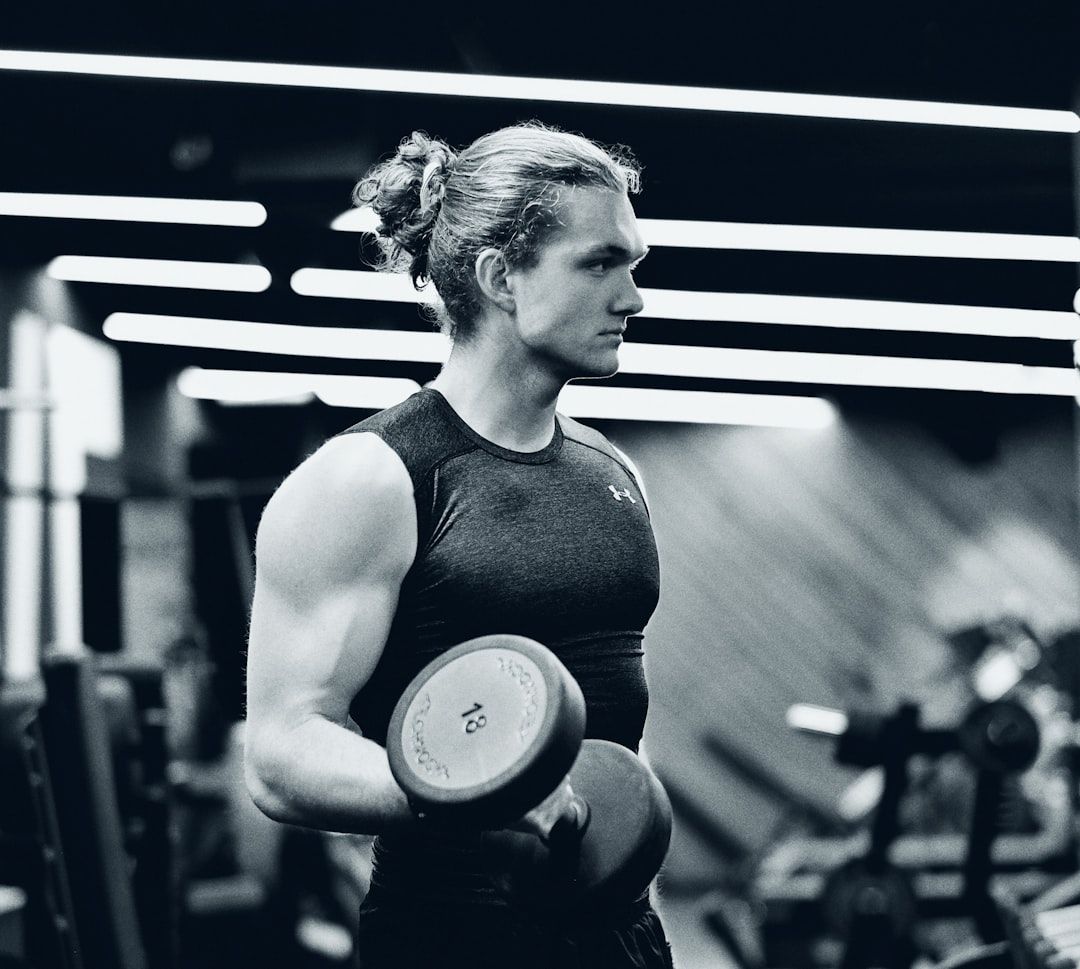 Man i träningslinne som utför bicepcurls med tunga hantlar på ett gym.